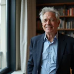 Portrait d'un journaliste élégant aux cheveux gris dans un appartement parisien moderne, illustrant la vie privée d'une personnalité médiatique
